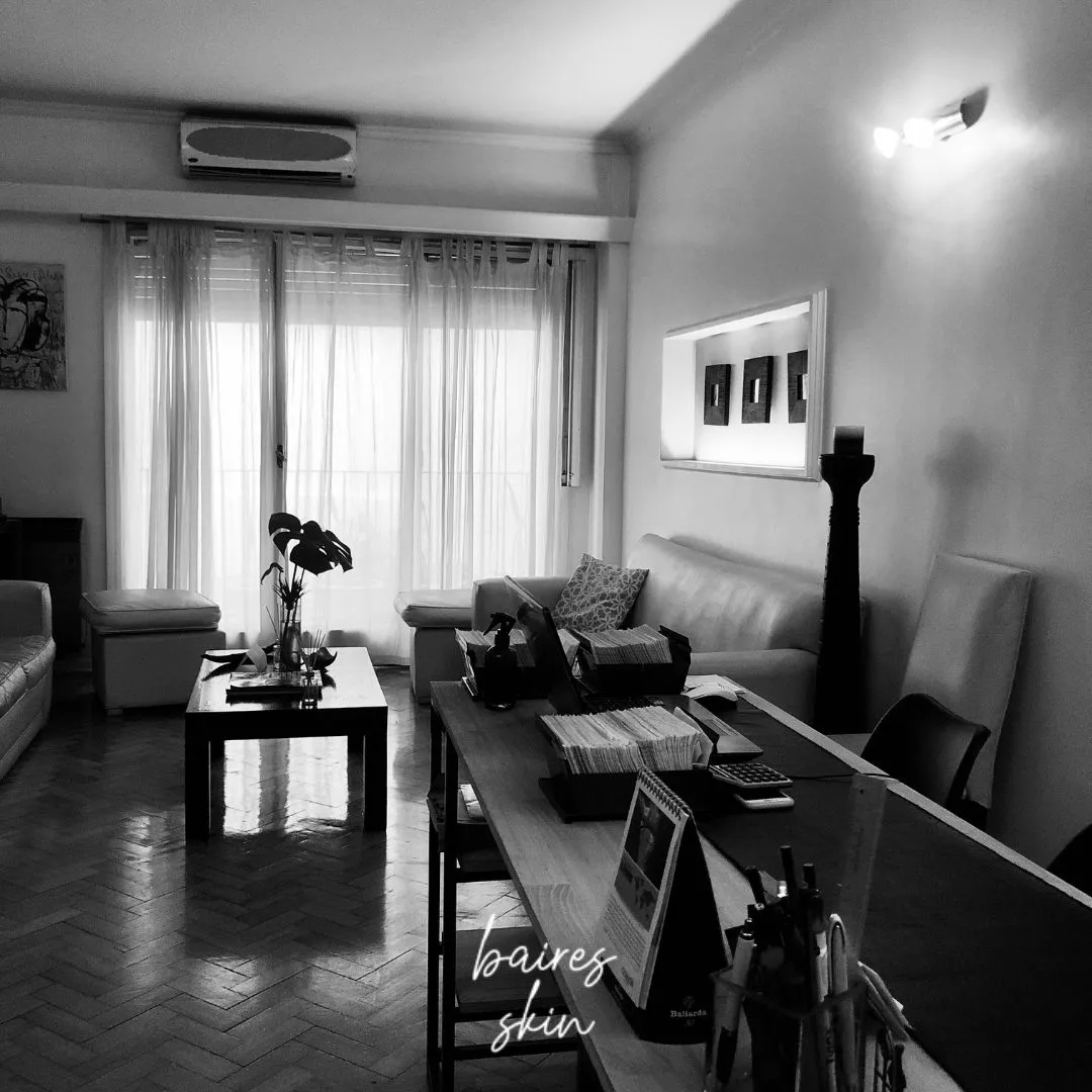 La sala de espera de Baires Skin en blanco y negro: sillones, mesa ratona con una planta, ventanal con cortinas y el escritorio de recepción